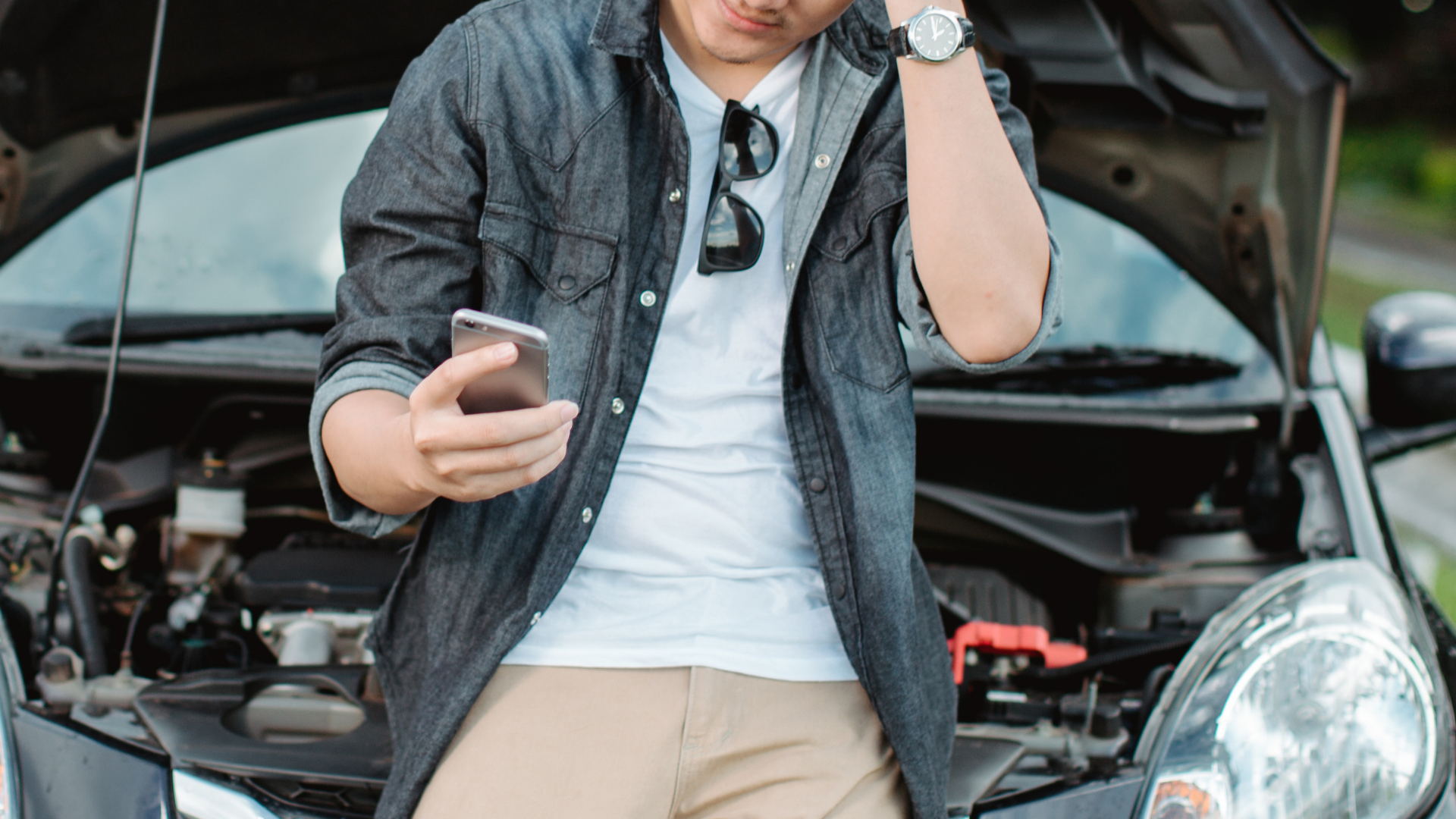 Car breakdown on a Malaysian highway with emergency services being contacted, safety measures like hazard lights and warning triangles in place, and the Motorist app displayed on a smartphone for roadside assistance.