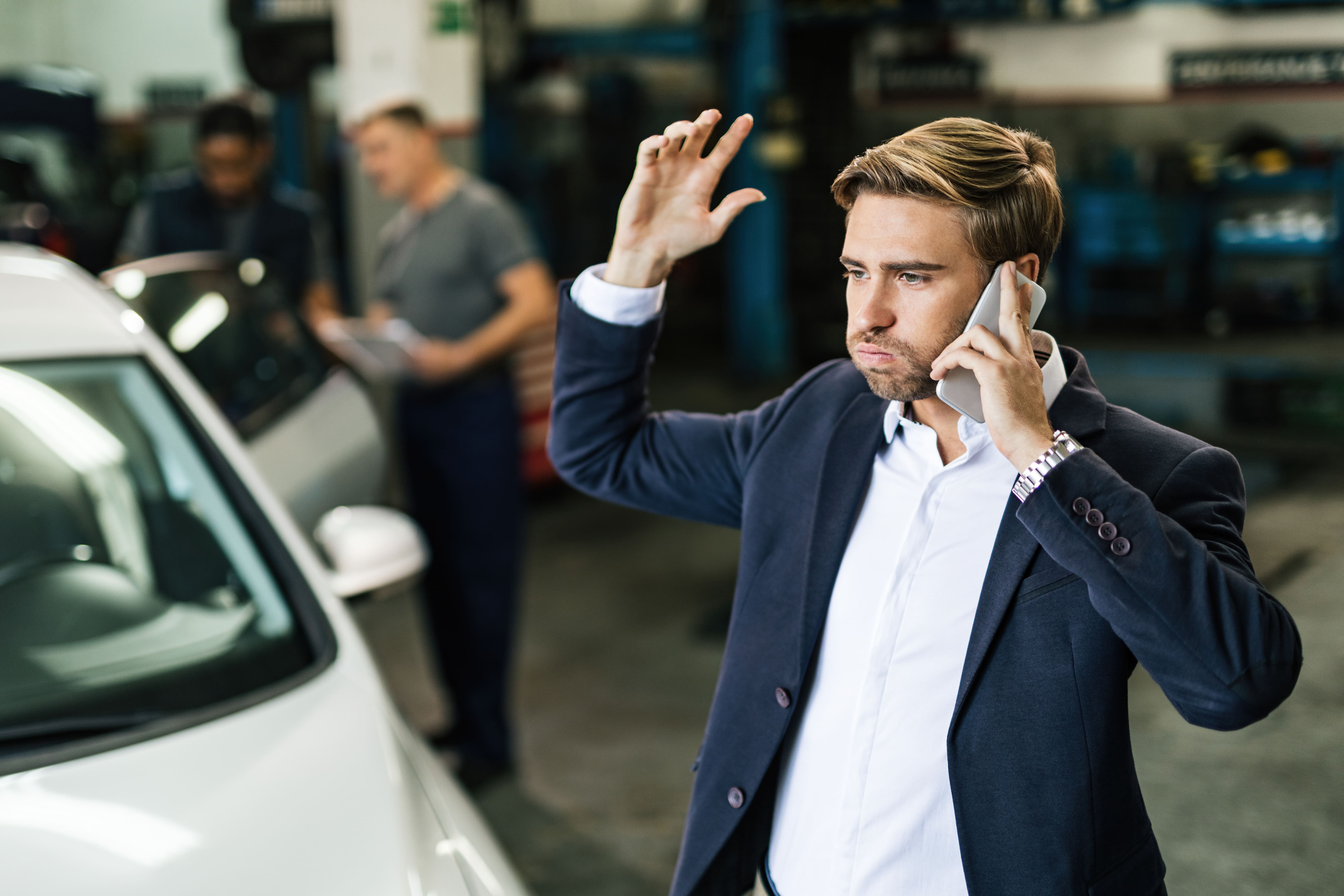 Editors%2 Fimages%2 F1766465107397 Young Displeased Businessman Talking Phone While Being Car Repair Workshop Min