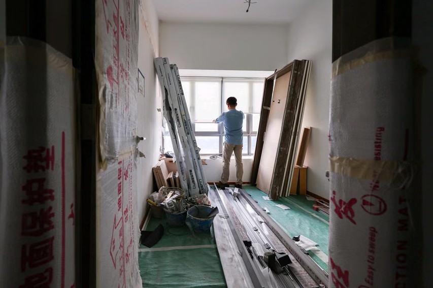 A man is looking outside while renovating a small room filled with construction materials and equipment.