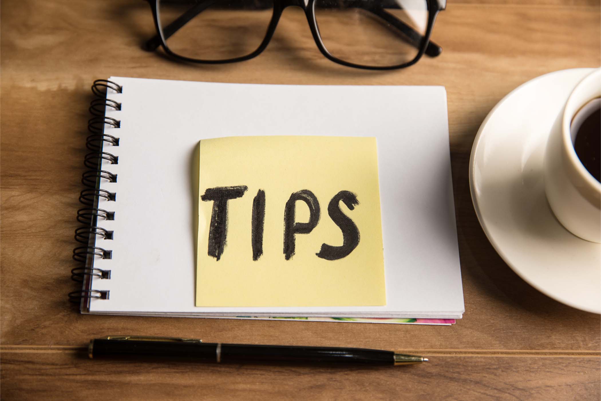 Sticky note labeled 'TIPS' placed on a notebook with writing tools and coffee nearby