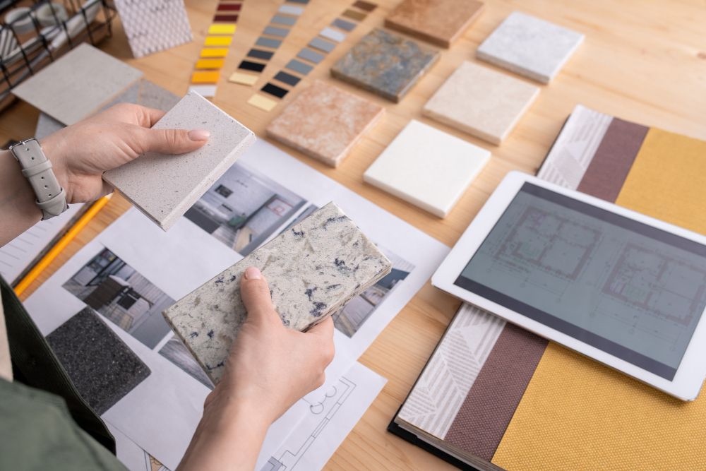 Interior designer selecting countertop samples with floor plan on tablet, color swatches, and material tiles.