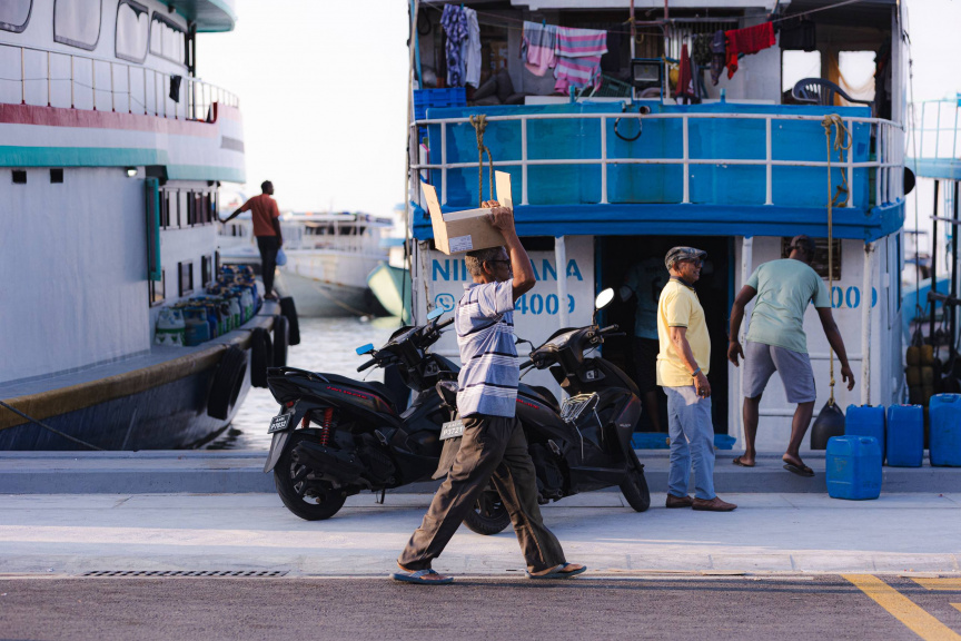މުދާ އުފުލާ ބޯޓެއް ކައިރިން މީހަކު ދަނީ: ރޯދަމަހަށް ރަށްރަށުން ކަރާ ފަދަ ތަކެތި އާންމުކޮށް ގިނަ އަދަދަކަށް ފޮނުވާ -- ސަން ފޮޓޯ/ ހުސައިން އާއިޝް އަޝްރަފް