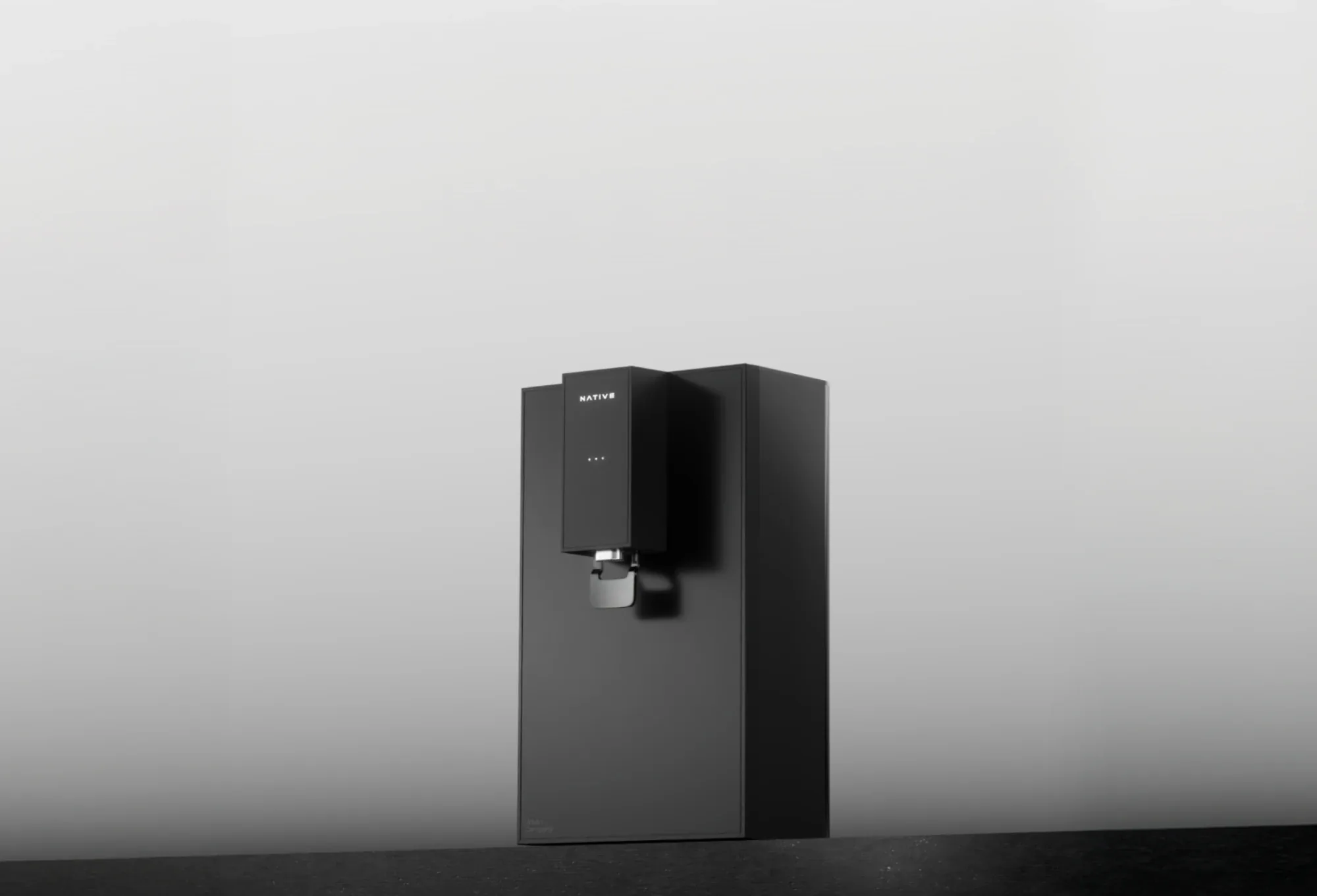 A black Native M0 water purifier standing on a dark counter against a soft grey studio background.